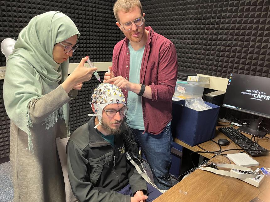 Ph.D. student Donnie Dunagan sits for a test-run as Dr. Dustin Chacón and Ph.D. student Hareem Khokhar dispense saline on cap sensors.