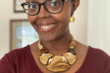 Image of Joy Peltier smiling wearing glasses and a statement necklace.